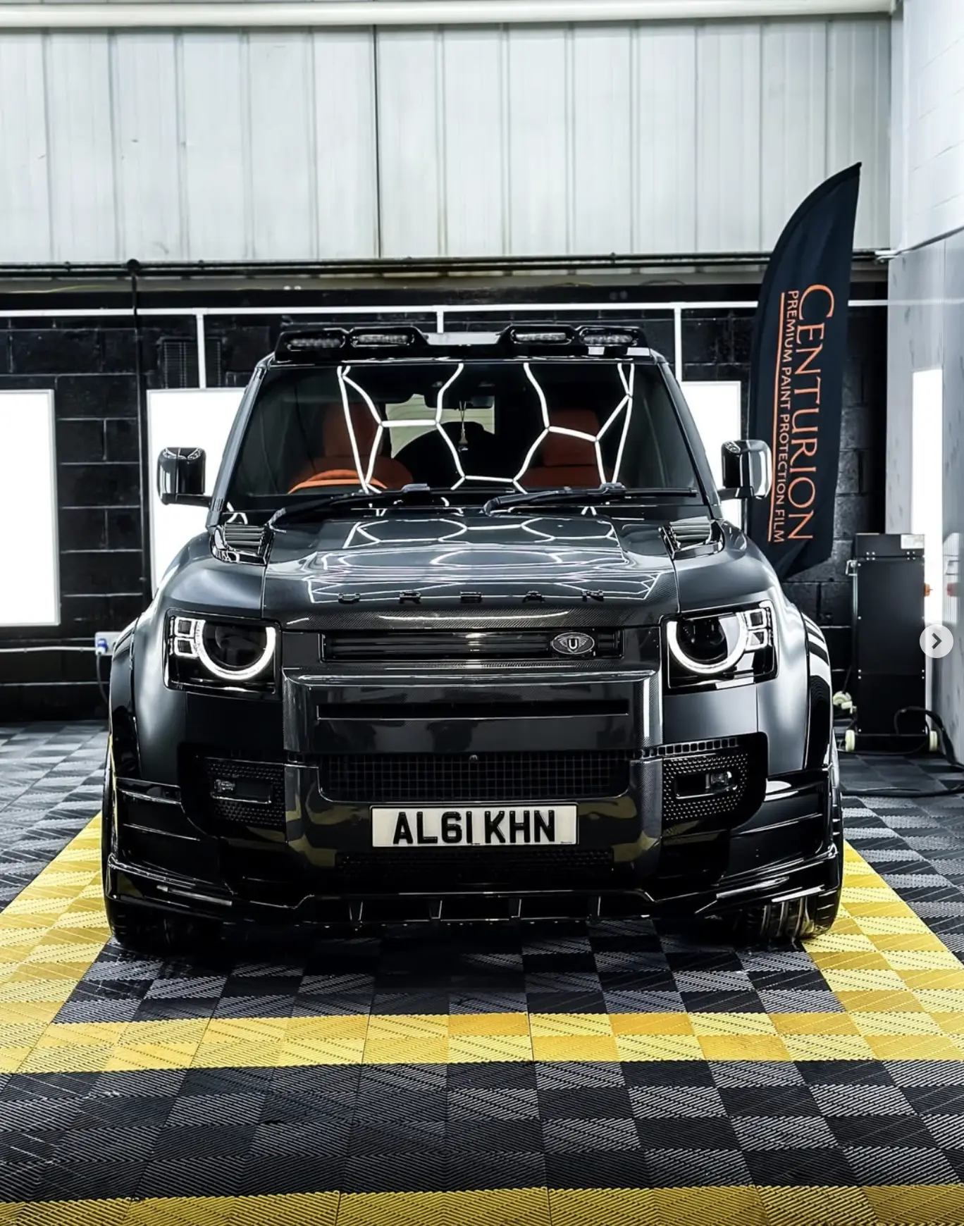 Urban Defender finished in gloss black Centurion PPF, photographed in The Wrap Lab bay beside a Centurion Premium Paint Protection Film banner.